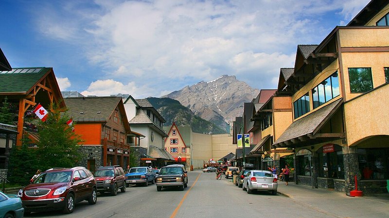 Banff town street lined with shops and Canadian flags beneath a Rocky Mountain peak.