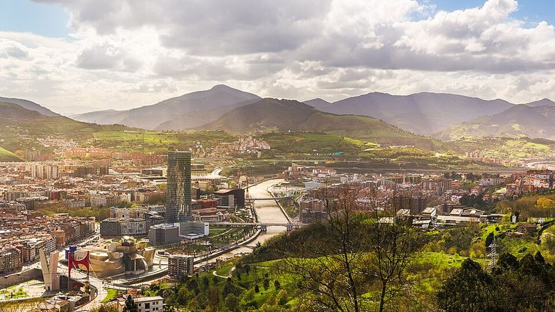Cityscape of Bilbao, Spain, surrounded by green hills.
