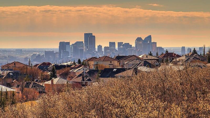Calgary downtown skyline beyond neighbourhood rooftops under a golden evening sky.
