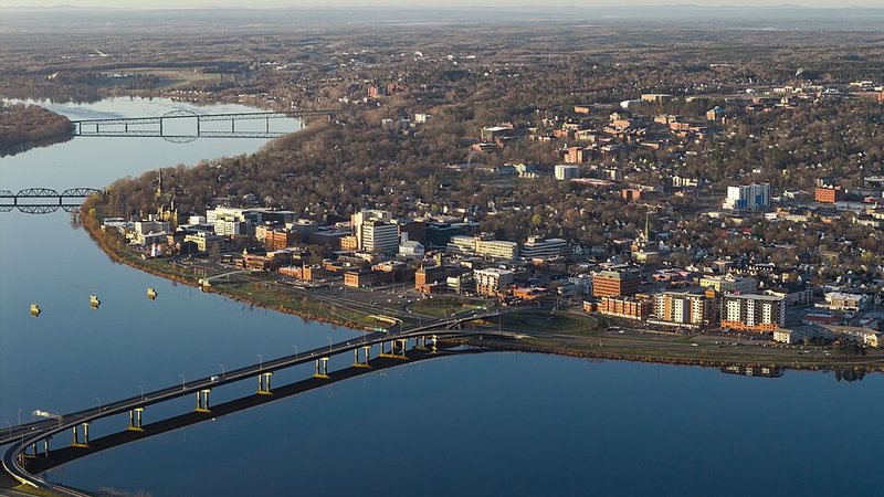 Aerial view of Fredericton beside the Saint John River, with bridges and downtown buildings.