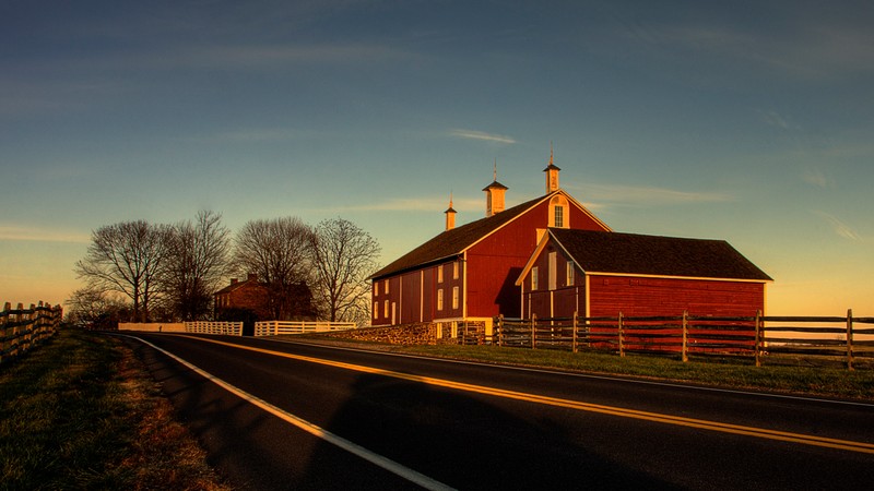 The red Codori farm barn and fences beside Emmitsburg Road on the Gettysburg battlefield, lit by low evening sun.