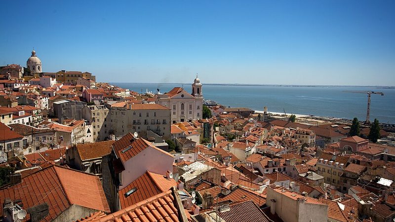 Terracotta rooftops of Lisbon's Alfama district above the Tagus River.