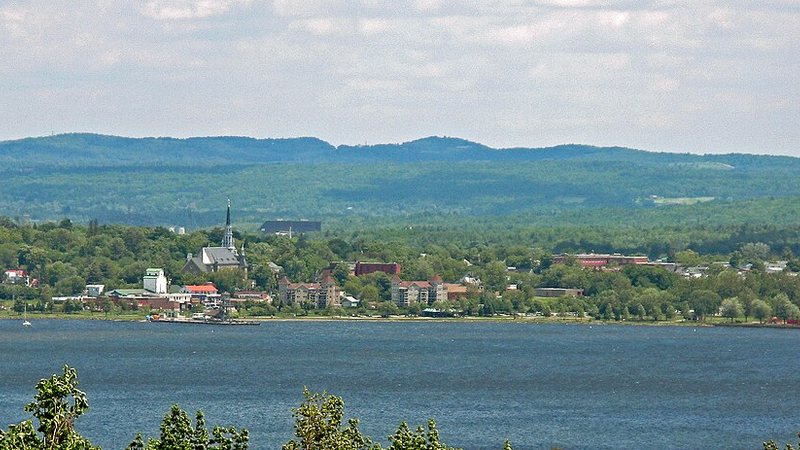 Magog waterfront and church spire across the lake, with forested hills behind the town.