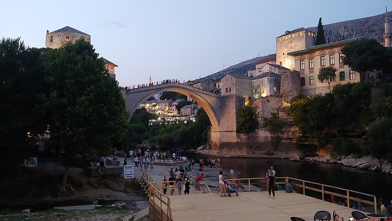 Mostar's Old Bridge and the riverside beach at sunset.