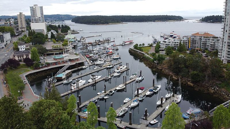 Boats in Nanaimo's downtown marina with waterfront buildings and forested islands beyond.
