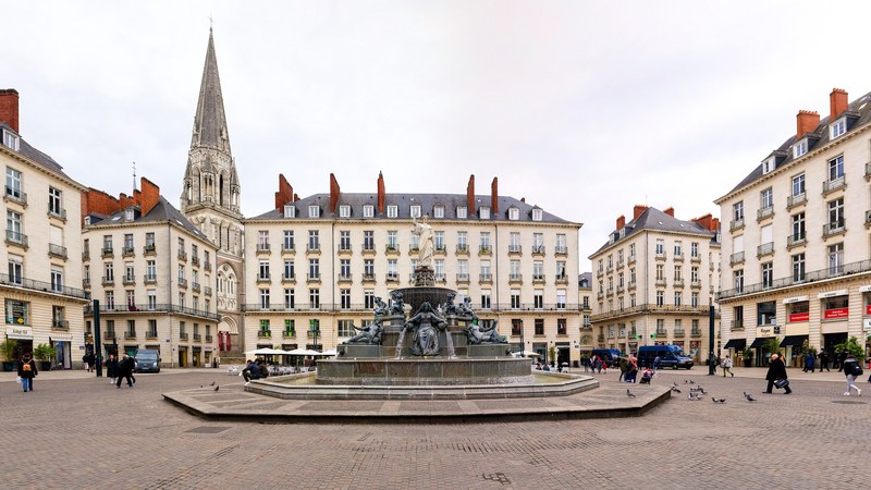 Place Royale in Nantes with its 19th-century fountain, cream stone neoclassical buildings and the spire of the Basilica of Saint-Nicolas behind.