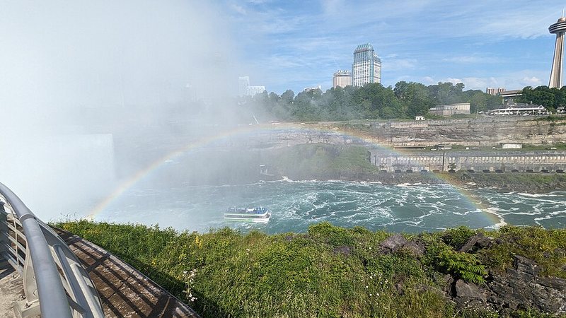 Rainbow in waterfall mist beside the Niagara River and Niagara Falls, Ontario skyline.