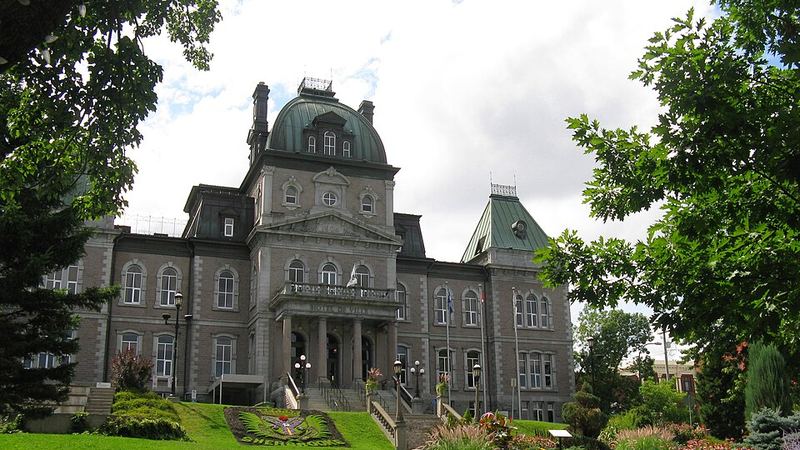Sherbrooke City Hall framed by leafy trees and landscaped gardens in summer.