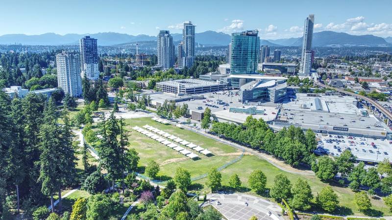 Aerial view over Holland Park toward the Surrey City Centre towers and the North Shore mountains on a sunny summer day, Surrey, British Columbia.